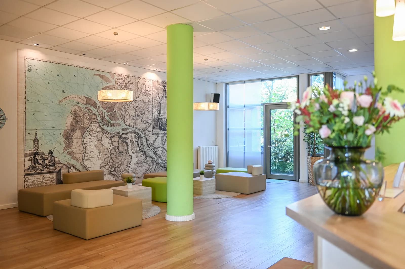 Lobby des Hotel NordRaum mit Sitzgruppe, grüner Säule und Blumenstrauß am Empfang