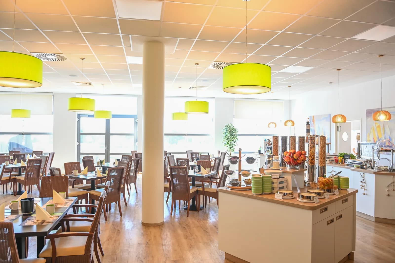 Heller Frühstücksraum mit Buffet, Holztischen und grünen Hängelampen